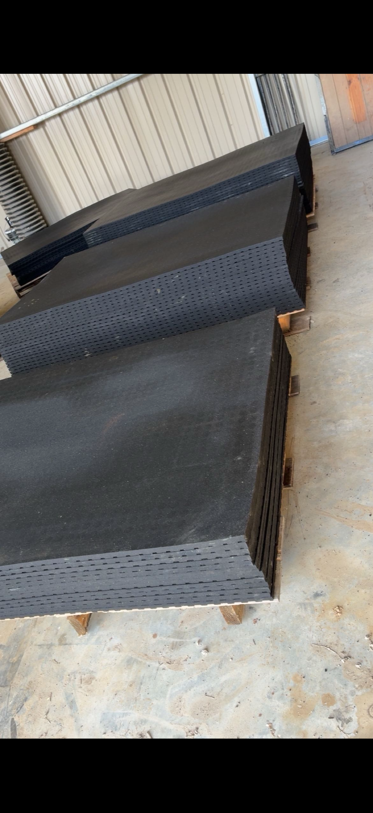 Stacked black rubber mats on pallets in warehouse